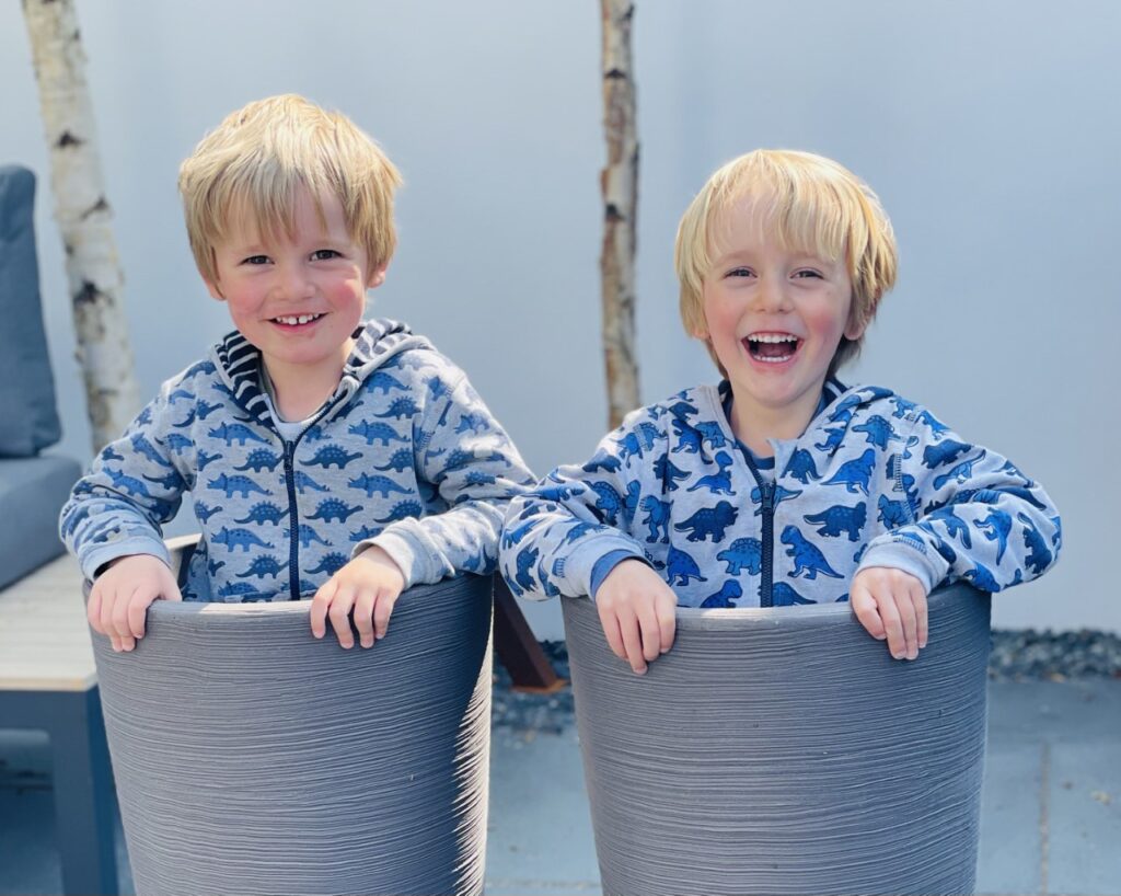 Twin three year old boys stand in plant pots in the garden playing during the pandemic