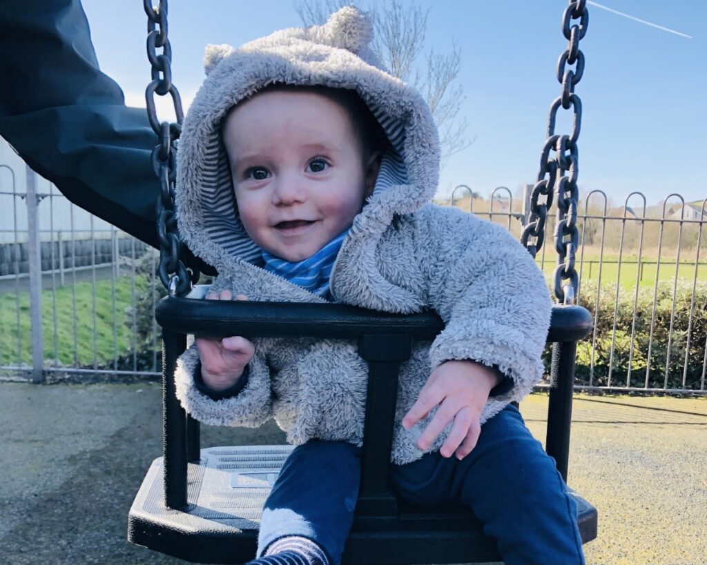 Nine month old baby in a bear fleece in a swing