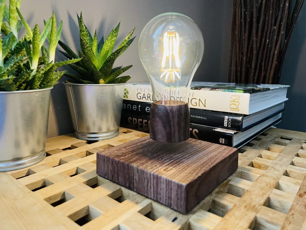 Volta levitating light bulb on a table next to books and cactus