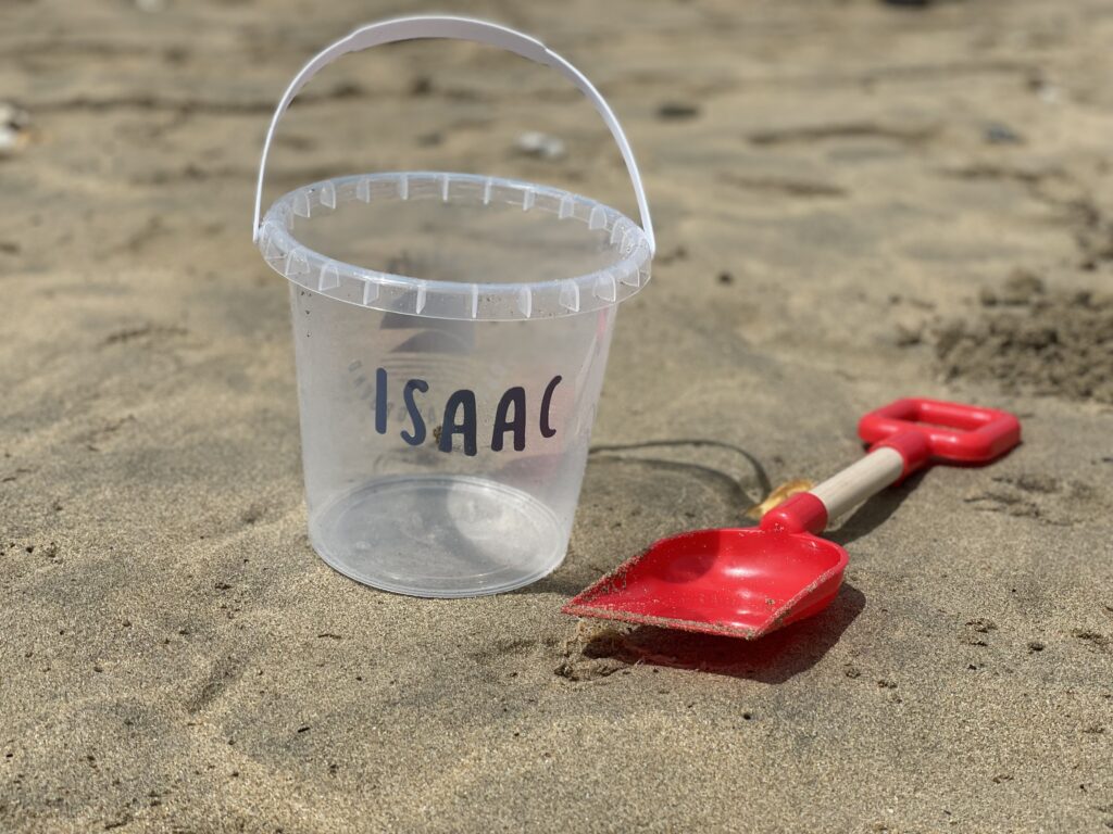 A personalised bucket and spade on a beach with the name Isaac on it.