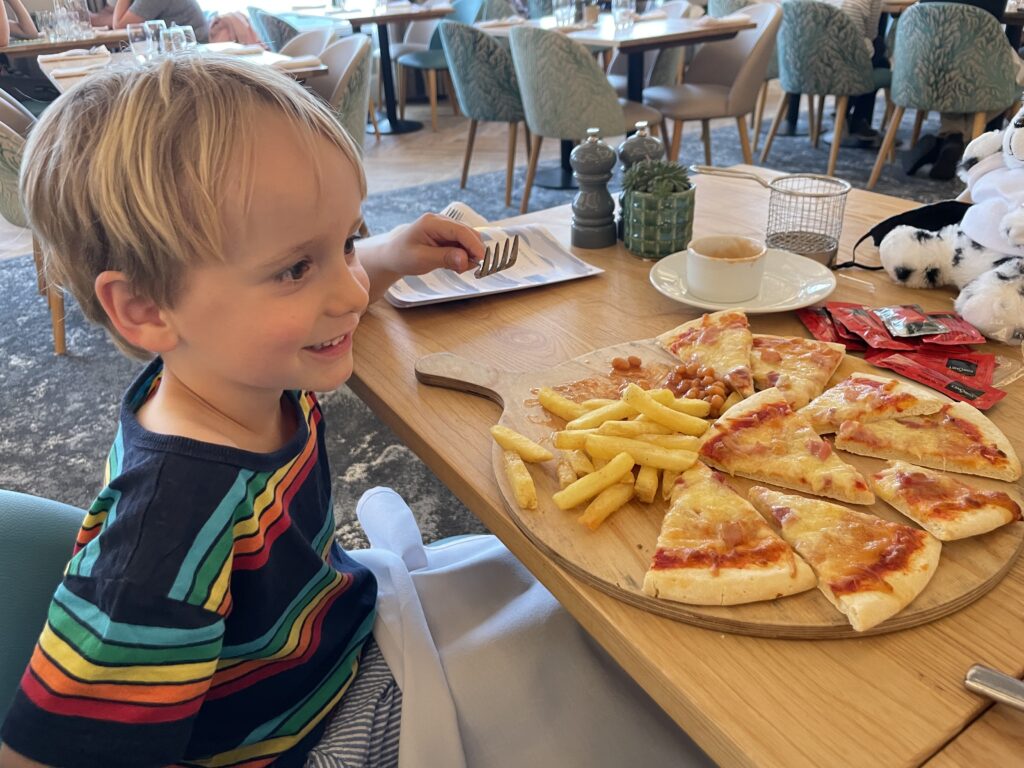 Four year old boy in stripy t shirt looks at a giant pizza in the restaurant of a family friendly hotel in Cornwall