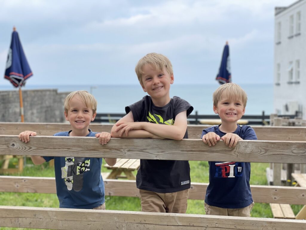 Three young brothers stand on a wooden wobbly bridge in a pirate play park at a family friendly hotel in cornwall