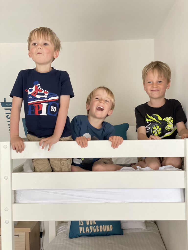 Four year old twins and six year old boy all sit on the top of a bunk bed