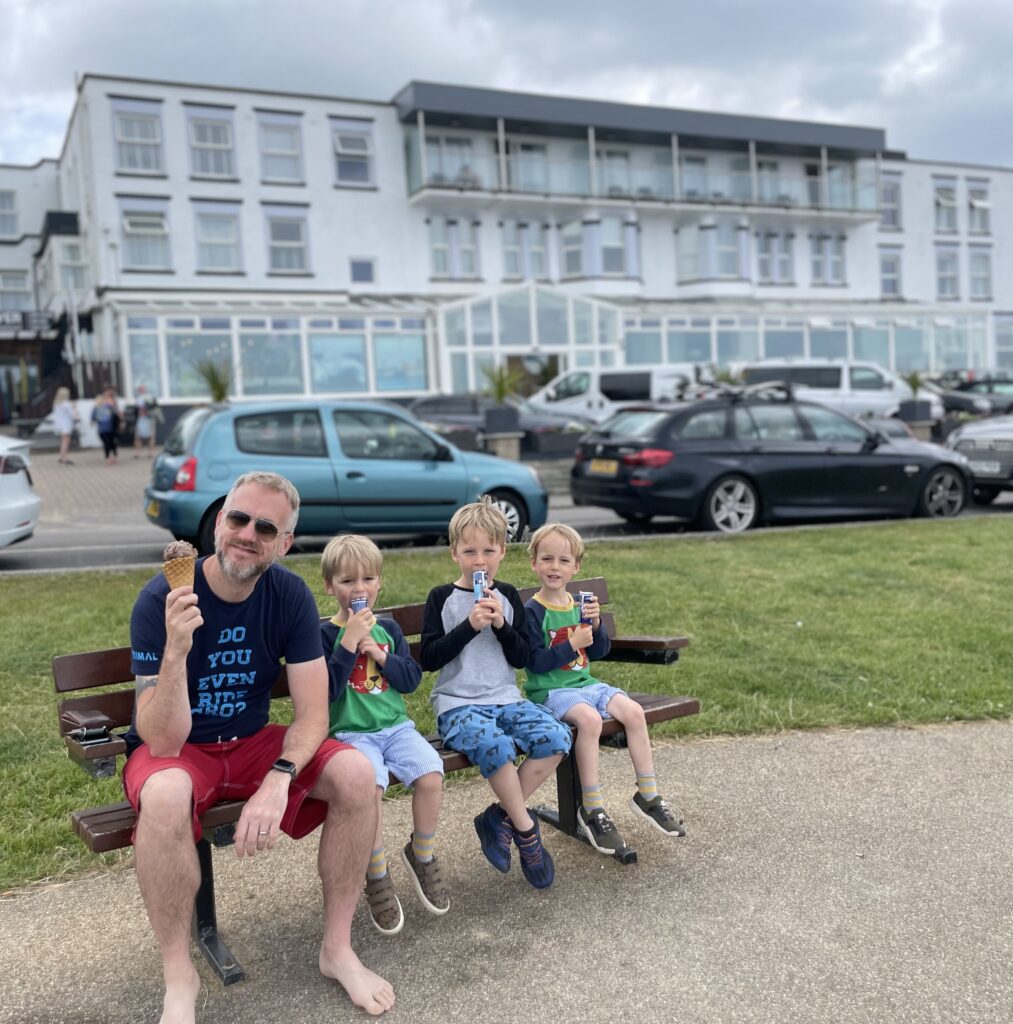 Three boys and their dad sit on a bench outside the Esplanade hotel in Newquay eating ice creams