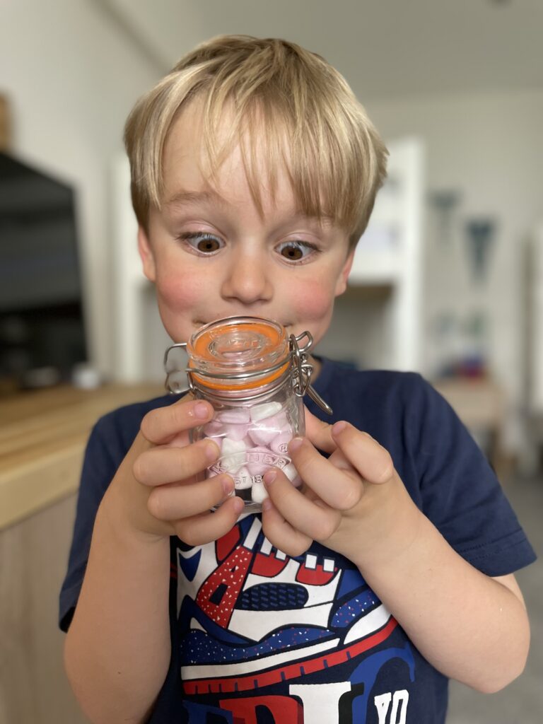 Four year old boy looking excitedly at a jar of mini marshmallows he's holding