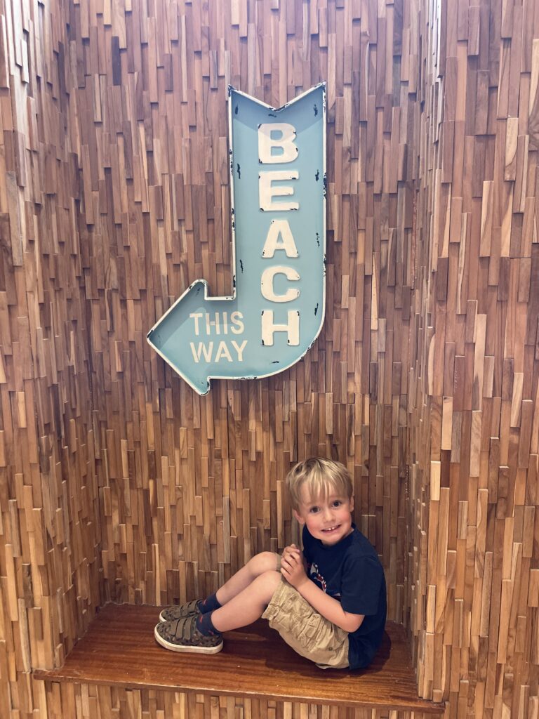 Four year old boy sits on a bench under a 'this way to the beach' sign at the Esplanade hotel in Newquay