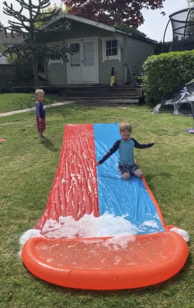 Little boys play on a slip n slide in the garden on a hot day