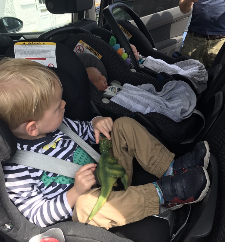 A toddler and newborn baby twins in the back seat of a car