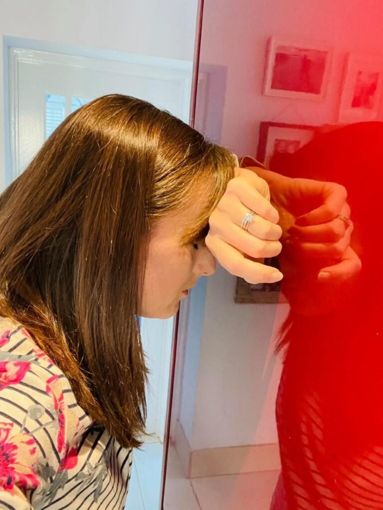 A mum with long brown hair has her head in her hand against the kitchen cabinet trying to be a calm parent