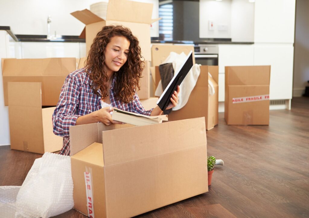 A woman with dark hair sits on the floor unpacking boxes after moving house