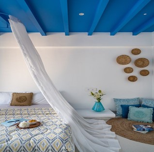 A greek styled bedroom with lots of white linen and blue wooden ceiling