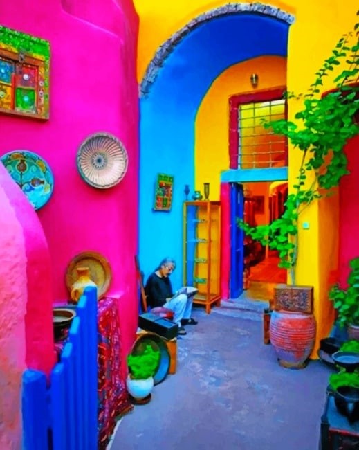 A lady sitting on a step surrounded by bright coloured walls in a Mexican style