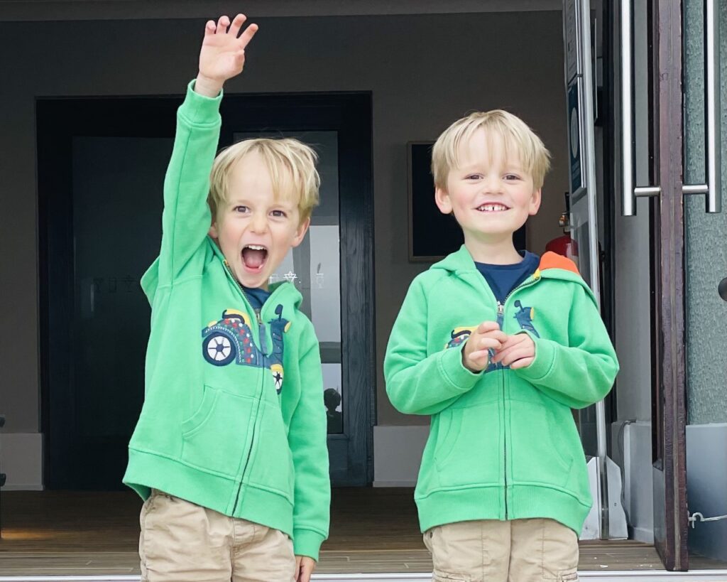 Four year old twin brothers wearing green hoodies smile and cheer in a hotel entrance