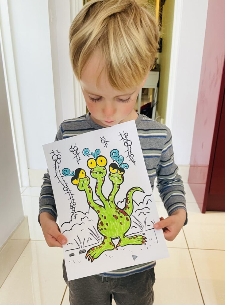 Four year old boy holds up a perfectly coloured in drawing of an octopus monster