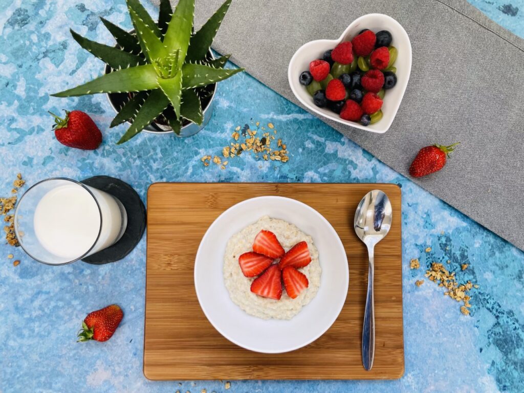 A blue flatlay with a breakfast of porridge containing good bacteria and a bowl of fruit