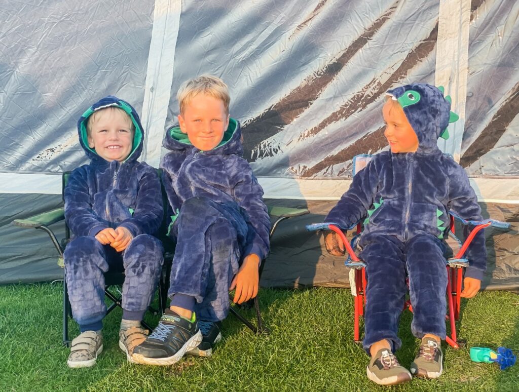 Brothers wearing dinosaur onesies sit outside a tent