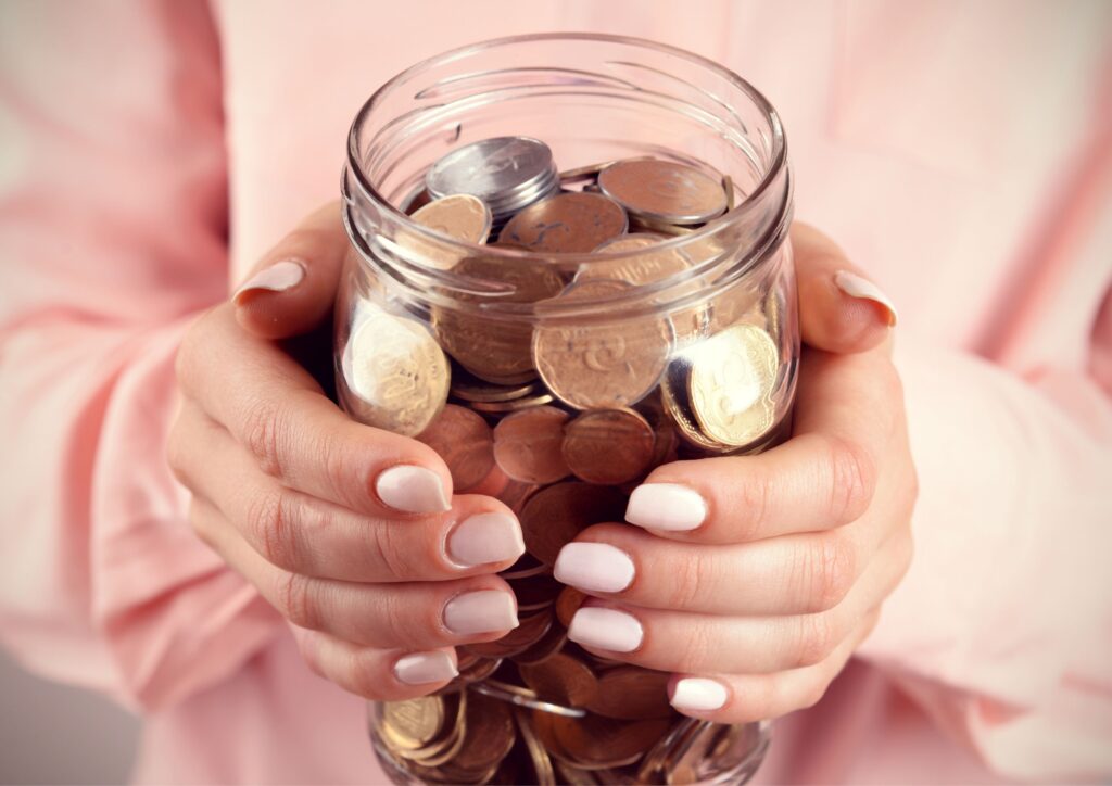 Woman's hands with pink nails holds a jar of coins for a post about financial habits and budgeting tips