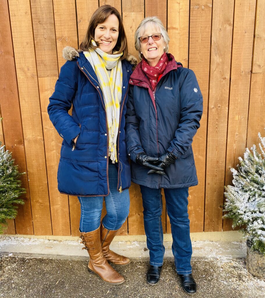 Mother and daughter in coats and scarves next to two little Christmas trees