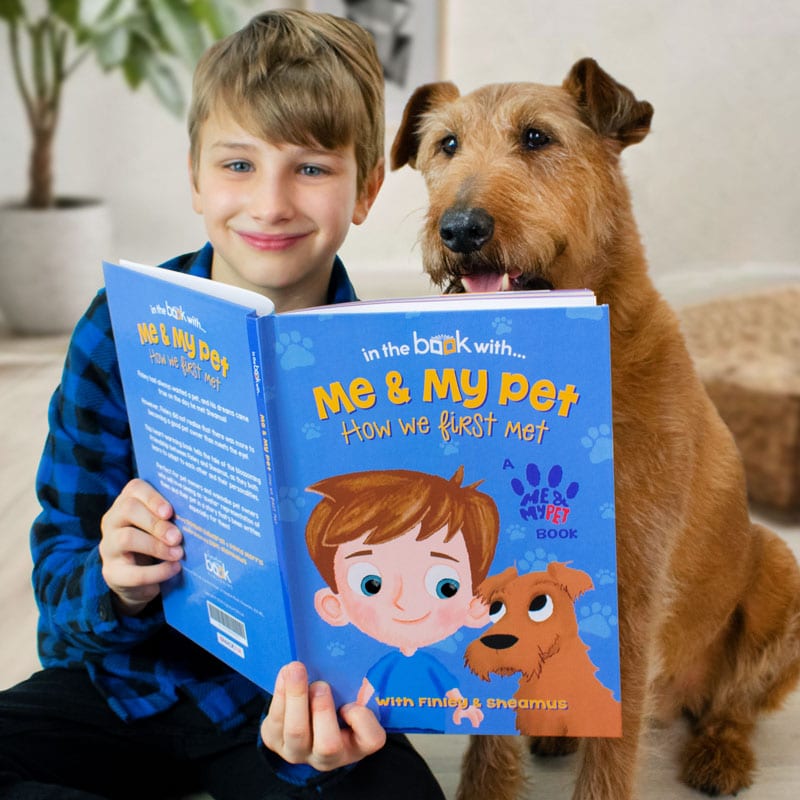 A boy reads a personalised children's book with his dog next to him about pets