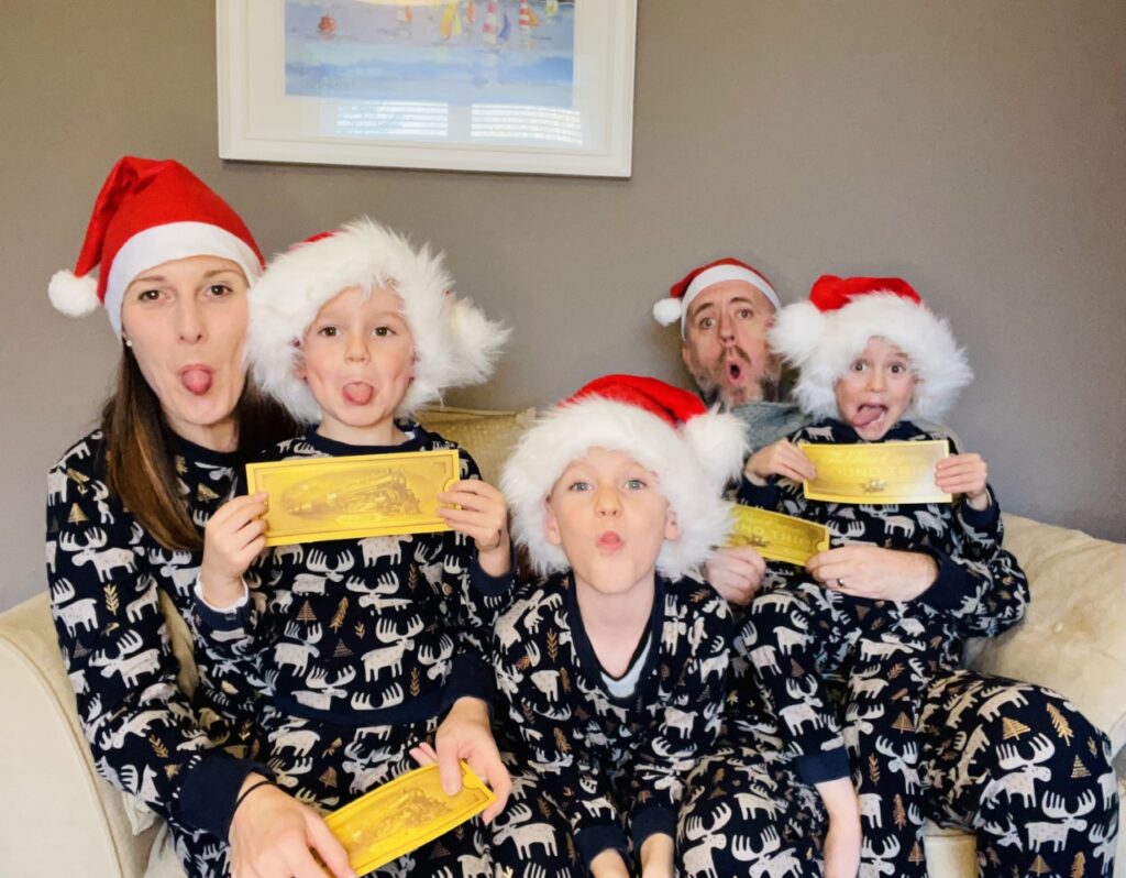 Family of parents and three boys wear santa hats and matching christmas pyjamas