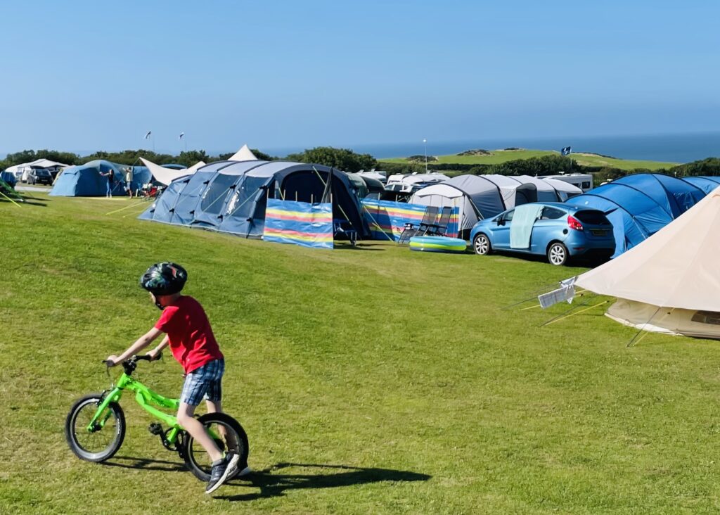 A boy on his bike on a campsite overlooking the sea for a list of camping essentials to pack