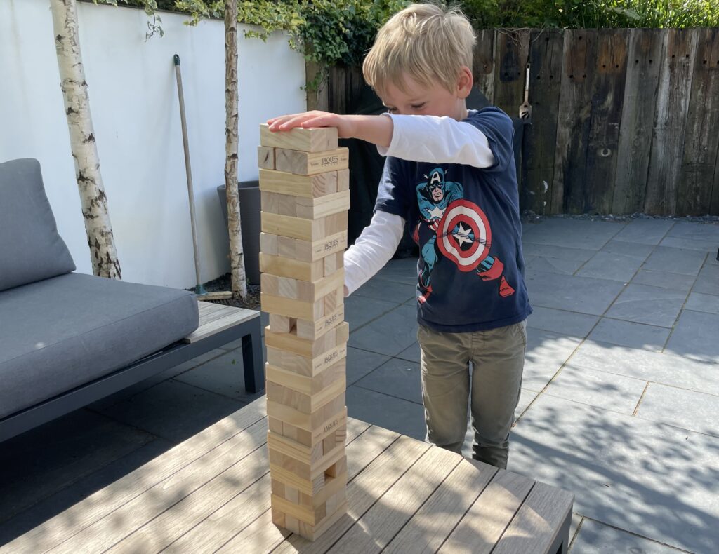 Four year old plays with wooden toys and a giant tumble tower on the patio