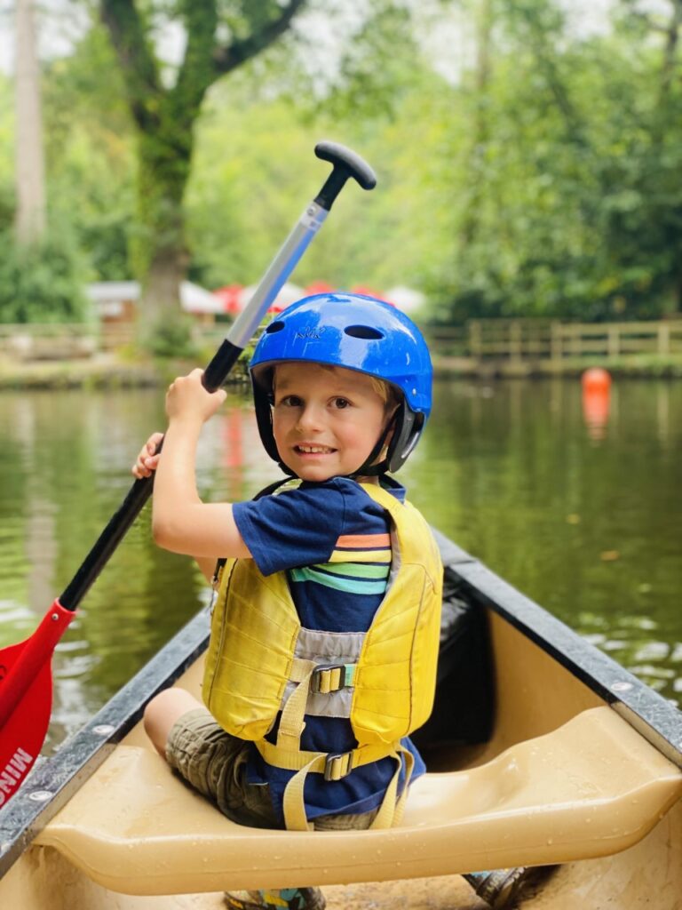 Five year old boy in life jacket and helmet paddling in a canoe