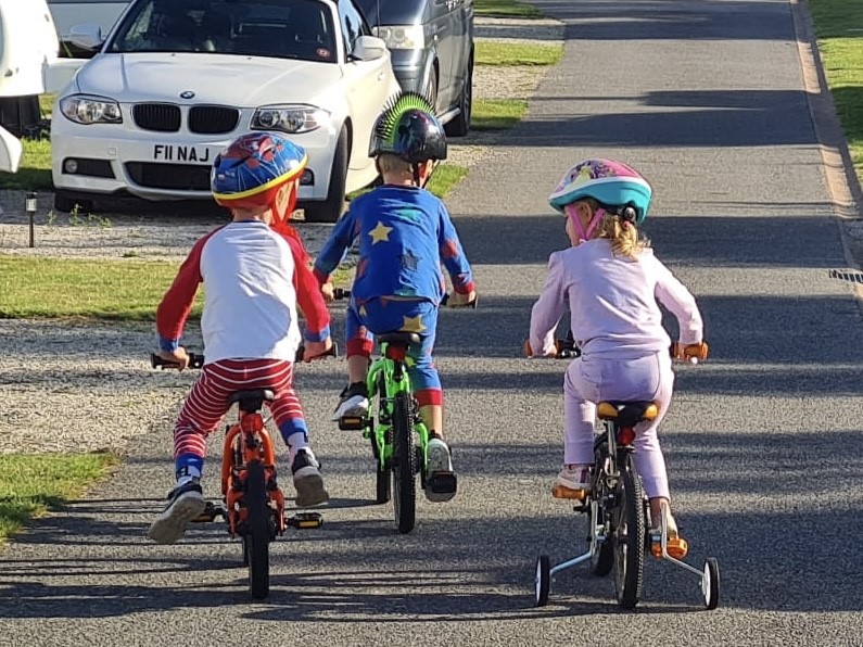 Cycling for kids is brilliant exercise, three kids cycle in their pyjamas at a camp site