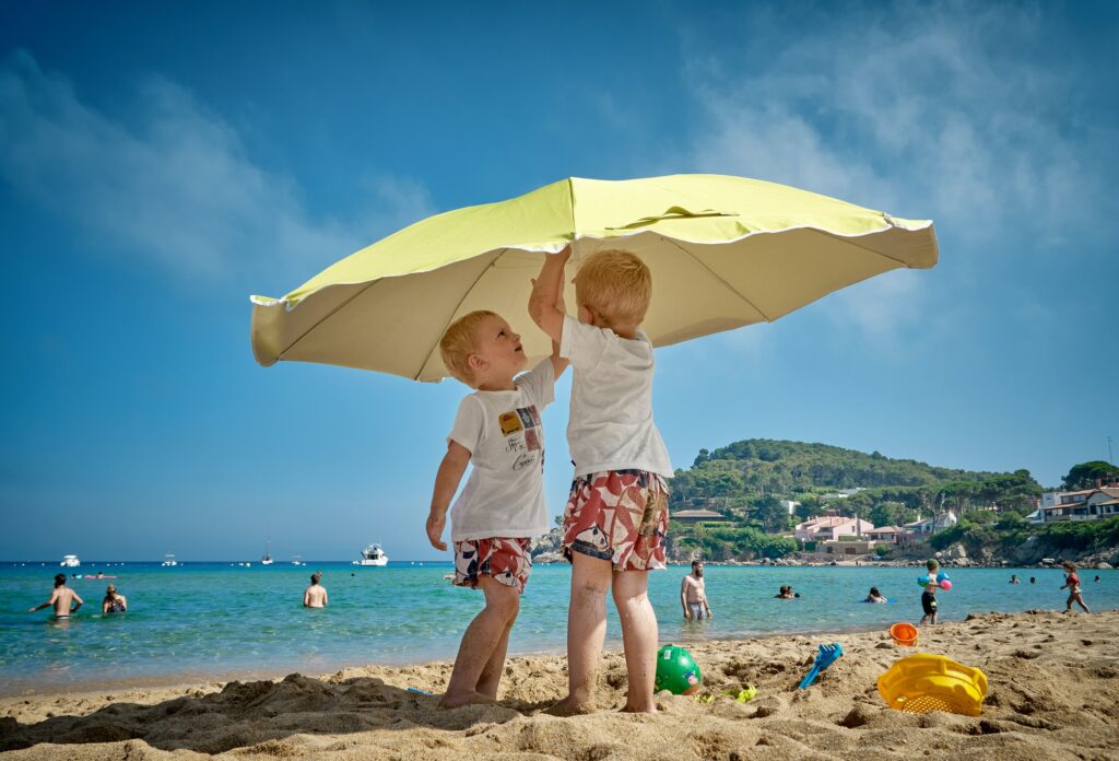 Two boys put up a parasol on a beach on a family holiday in Spain with kids