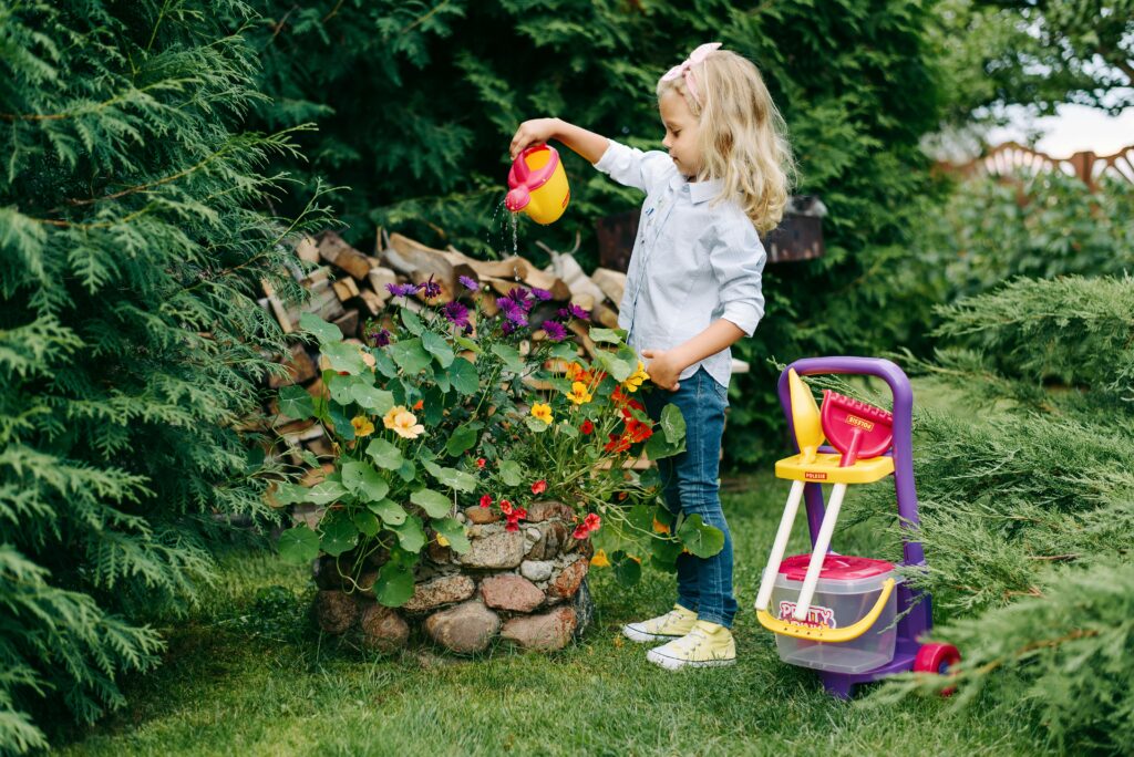 A blonde girl is watering the garden with a plastic watering can