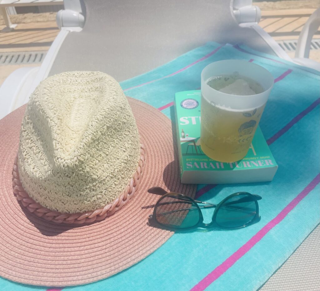 Sun hat, beer, sunglasses and book on a beach towel in the sunshine