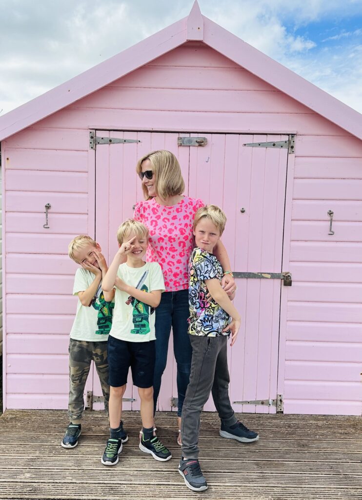 Helen and boys in front of a pink beach hut
