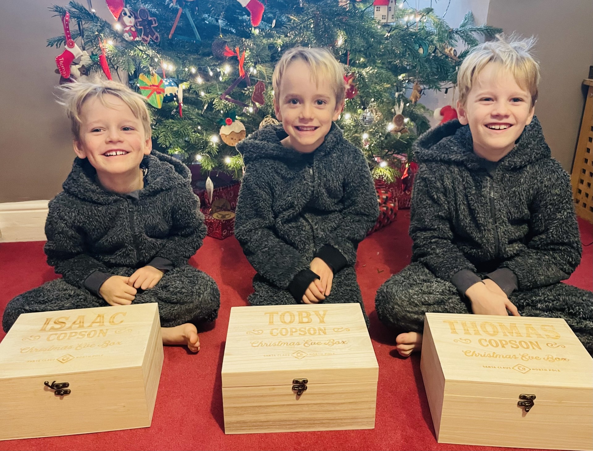 Three boys with their Christmas eve boxes in front of the tree as one of several Christmas traditions the family does
