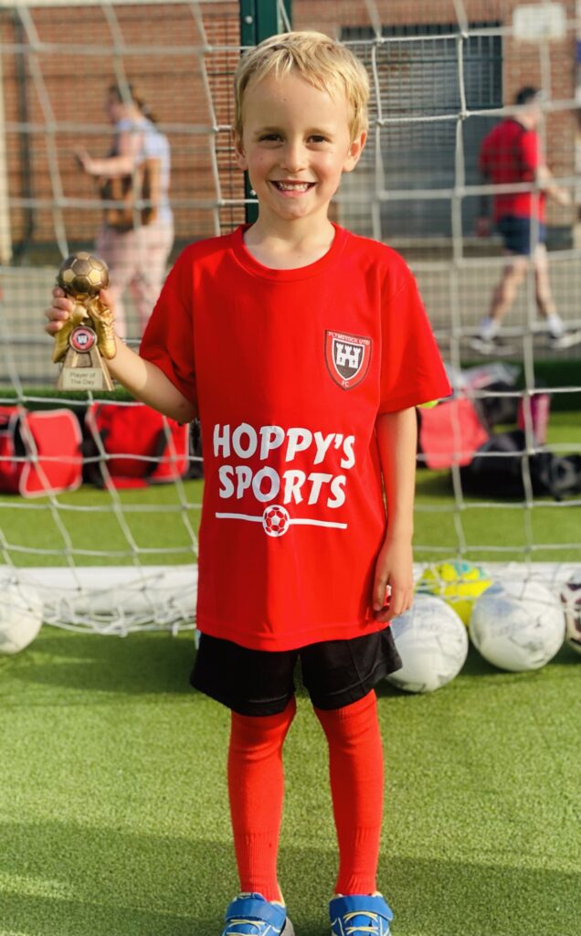 A little boy in football kit holding a trophy